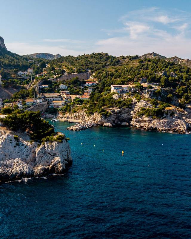 Falaises blanches plongeant dans une mer bleu profond, village de calanque en arrière-plan