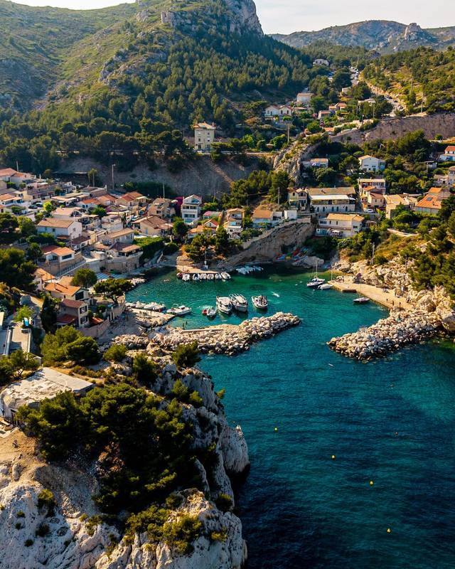 Petit port de calanque aux eaux turquoise entouré de maisons et de pins, vu du ciel