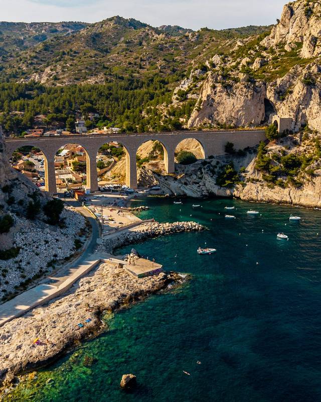 Calanque bordée de falaises calcaires, traversée par un viaduc ferroviaire en pierre