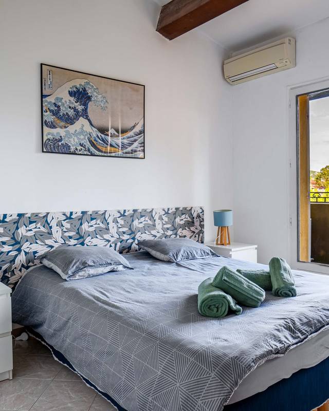 Chambre lumineuse avec lit double, estampe japonaise au mur et palmiers par la porte-fenêtre