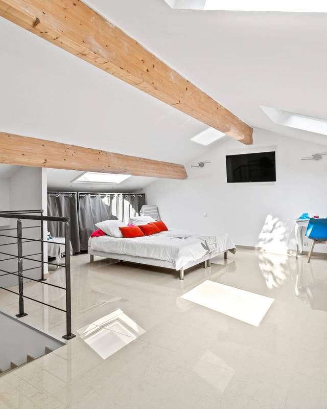 Chambre sous les toits avec poutres claires, garde-corps métallique et fenêtres de toit