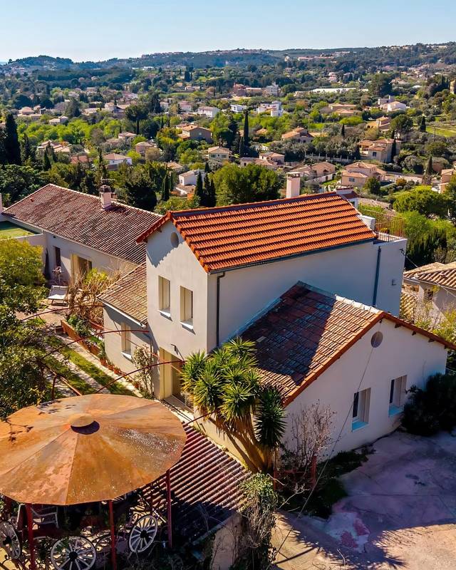 Maison individuelle aux tuiles rouges entourée de verdure, collines à l'horizon