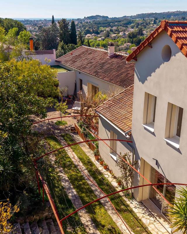 Façade d'une maison prise en hauteur, avec jardin en restanques et vue dégagée