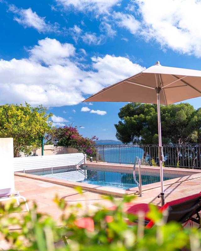 Terrasse avec piscine, parasol et vue sur la mer entre les pins