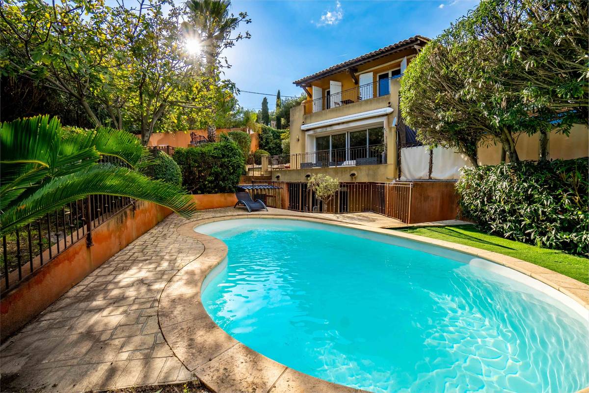 Piscine en forme de haricot bordée de palmiers devant une villa ocre