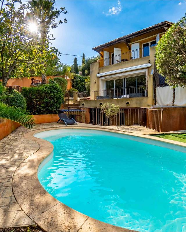 Piscine en forme de haricot bordée de palmiers devant une villa ocre