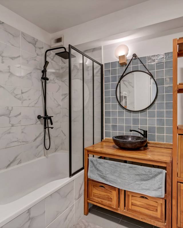 Salle de bains avec baignoire, paroi vitrée noire, meuble vasque et étagère en teck