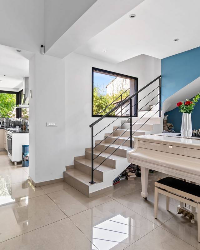 Séjour avec piano blanc, escalier à garde-corps métallique et mur bleu