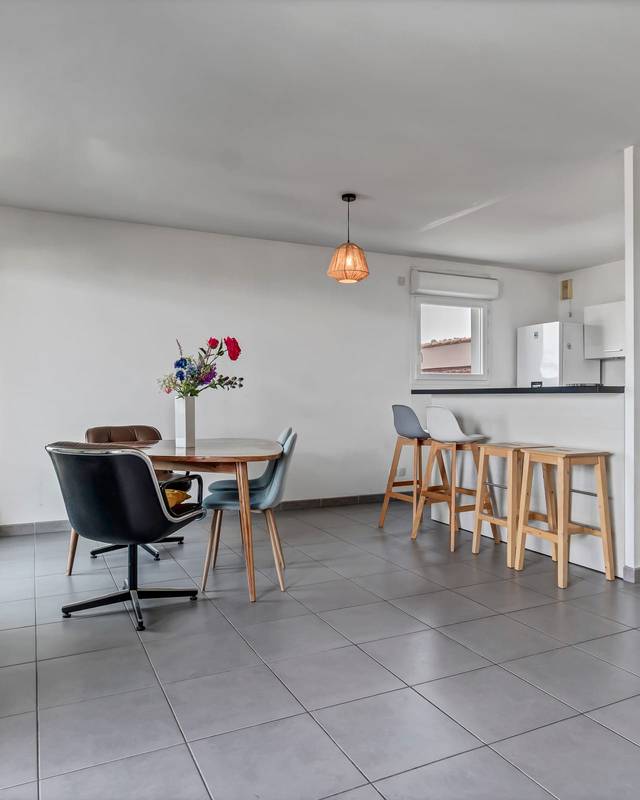 Séjour avec table ronde, chaises noires et bar ouvert sur la cuisine