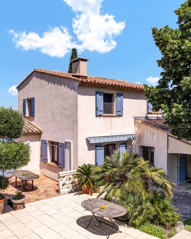 Villa aux volets lavande et sa terrasse ombragée, photographiée à faible hauteur